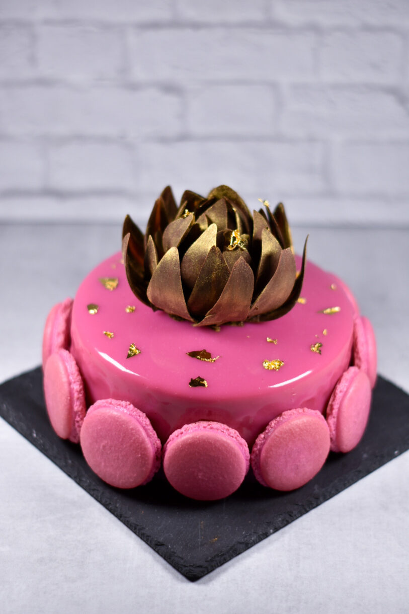 Passionfruit, coffee, and chocolate entremet decorated with chocolate rose, macarons, and gold leaf