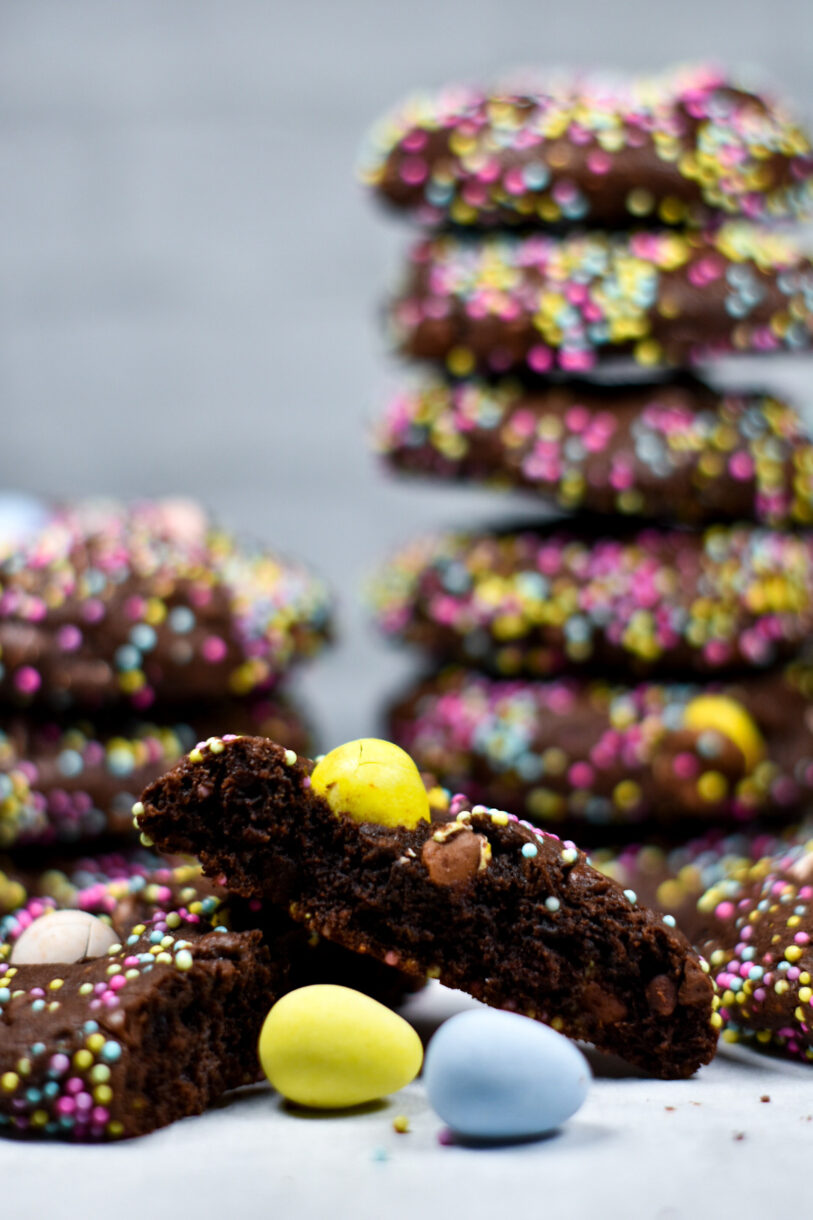 A sliced chocolate mini egg cookie and a stack of cookies in the background