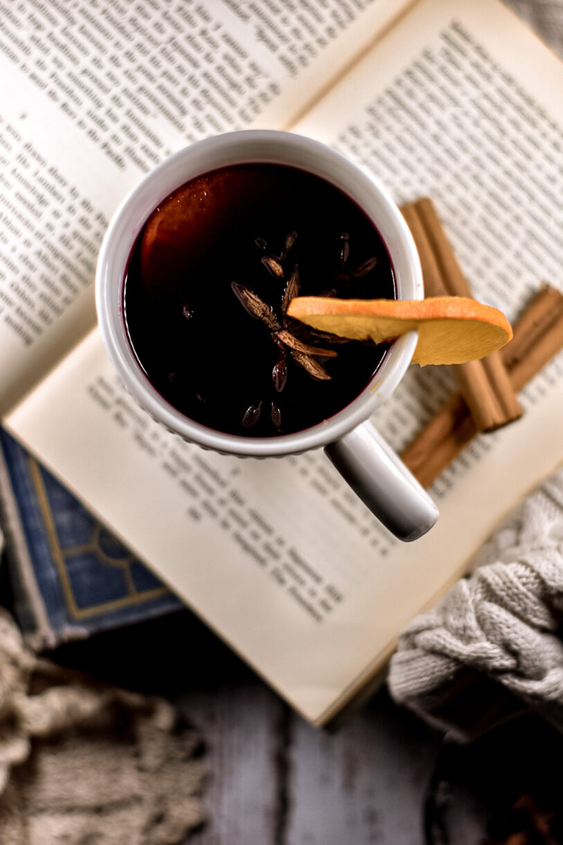 Closeup shot of a mug of mulled wine, next to two cinnamon sticks and sitting on top of an open book