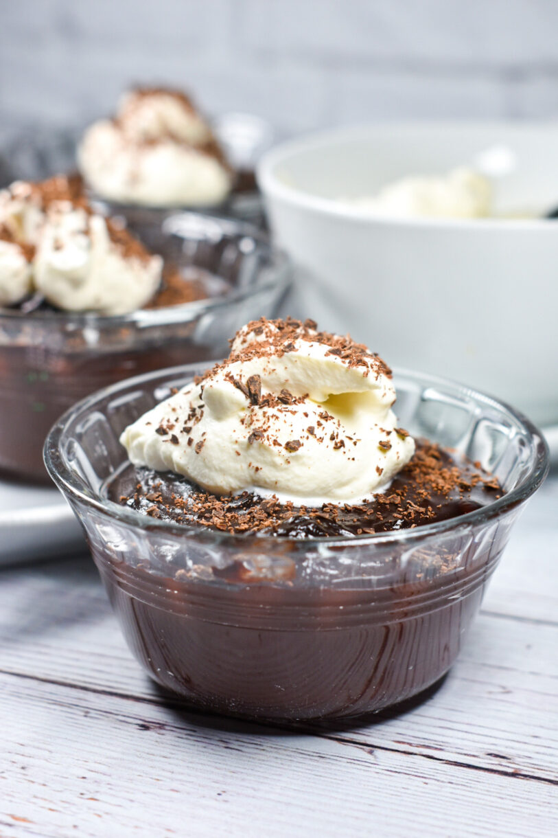 A glass bowl of chocolate pudding garnished with whipped cream and shaved chocolate
