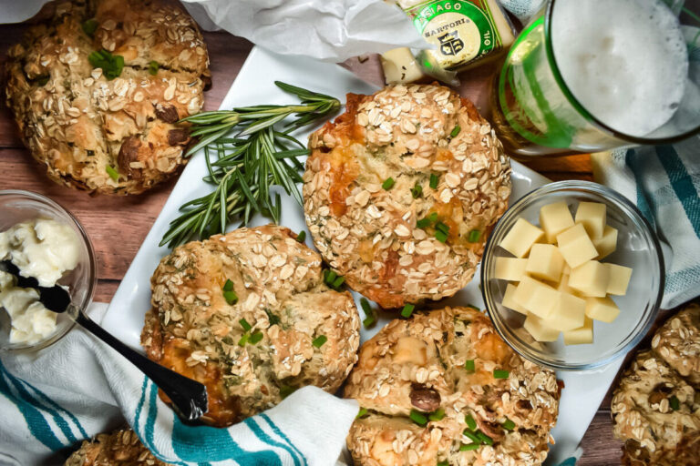 Miniature soda bread loaves on a rectanglar white plate, along with cheese, butter, and a mug of beer