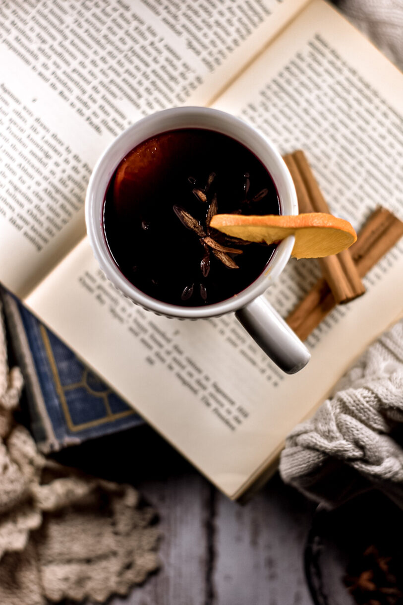 Looking down into a mug of mulled wine, with antique books and cosy fabrics surrounding it