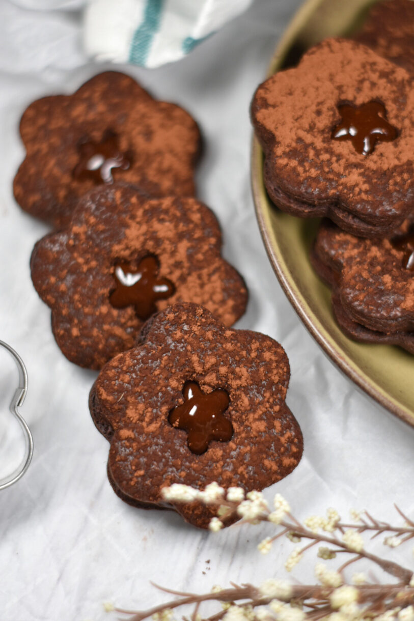 Flower shaped chocolate shortbread cookies with chocolate ganache, on a white surface