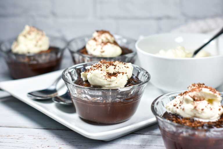 Bowls of chocolate pudding arranged on a white tray, along with spoons and a bowl of whipped cream