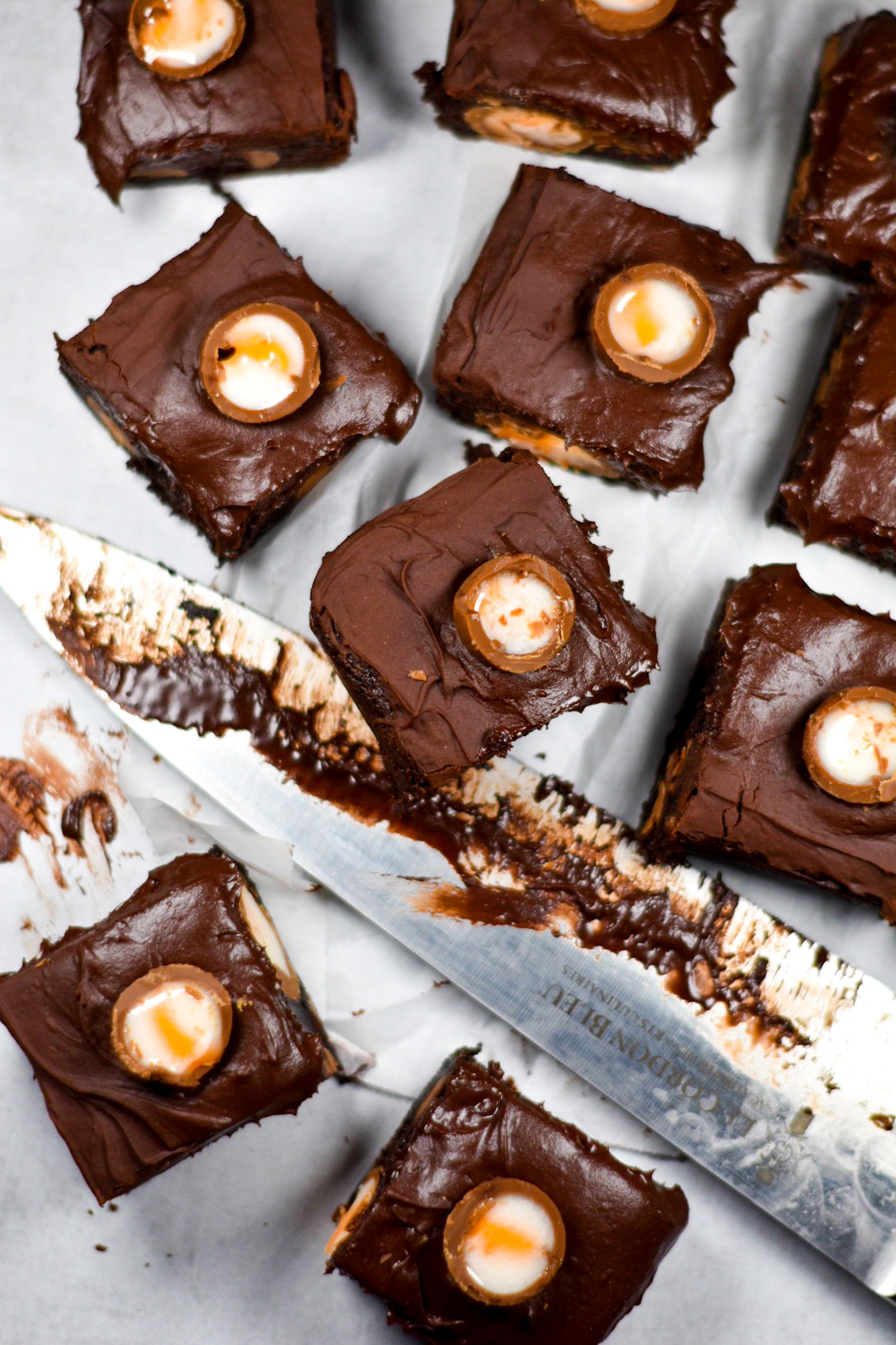 chocolate creme egg brownies and a frosting covered knife on a white surface