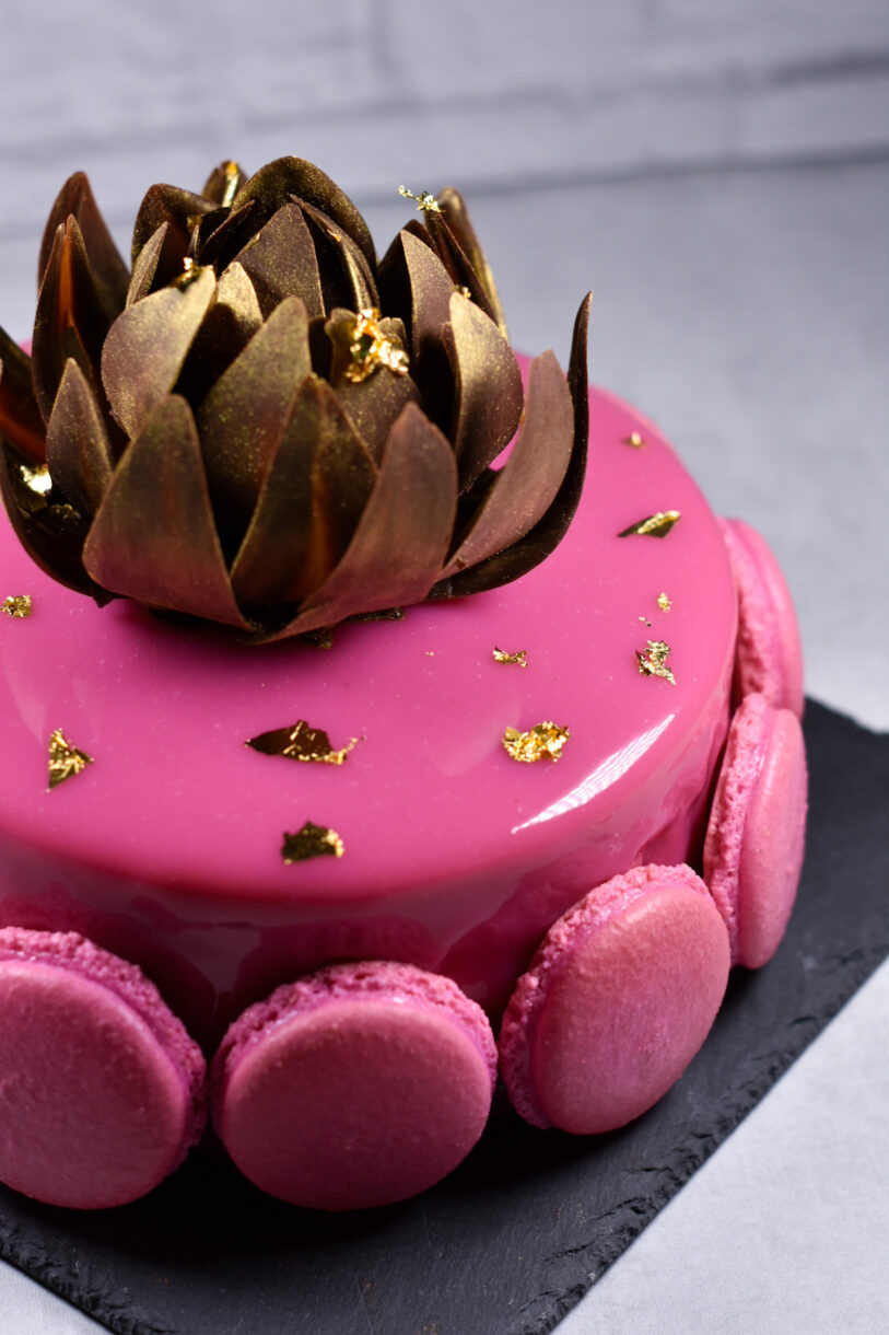Passionfruit, coffee, and chocolate entremet on a black slate board, adorned with macarons and gold chocolate rose