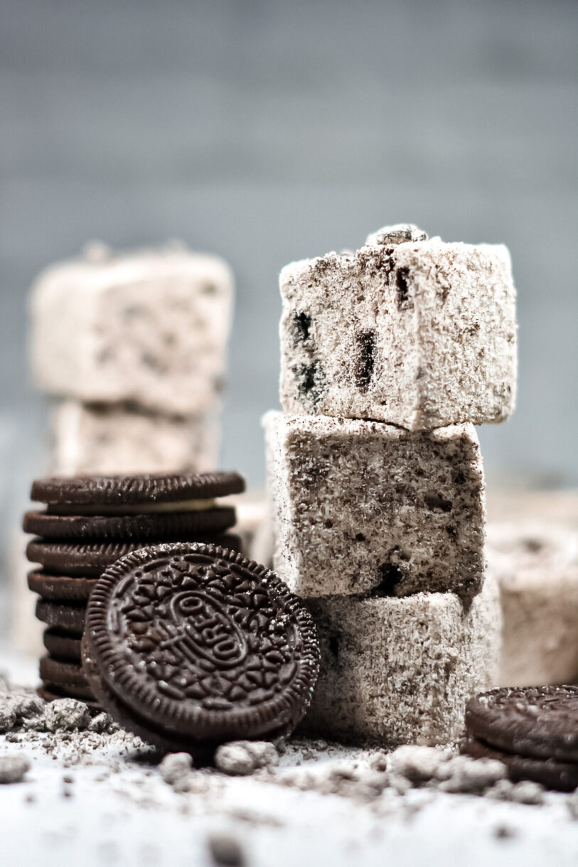 A stack of three cookies and cream marshmallows with a stack of Oreo cookies nearby