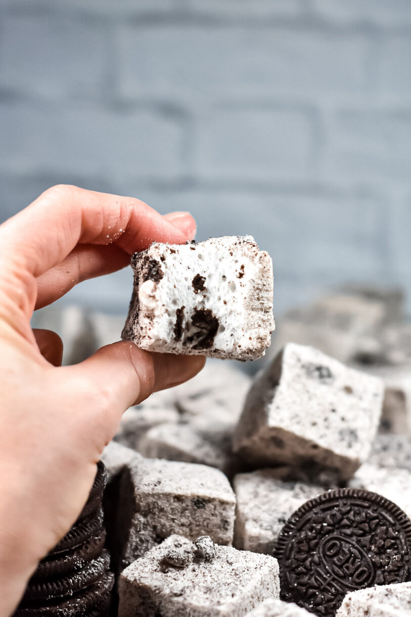 Hand squeezing an Oreo cookie marshmallow with a bite missing