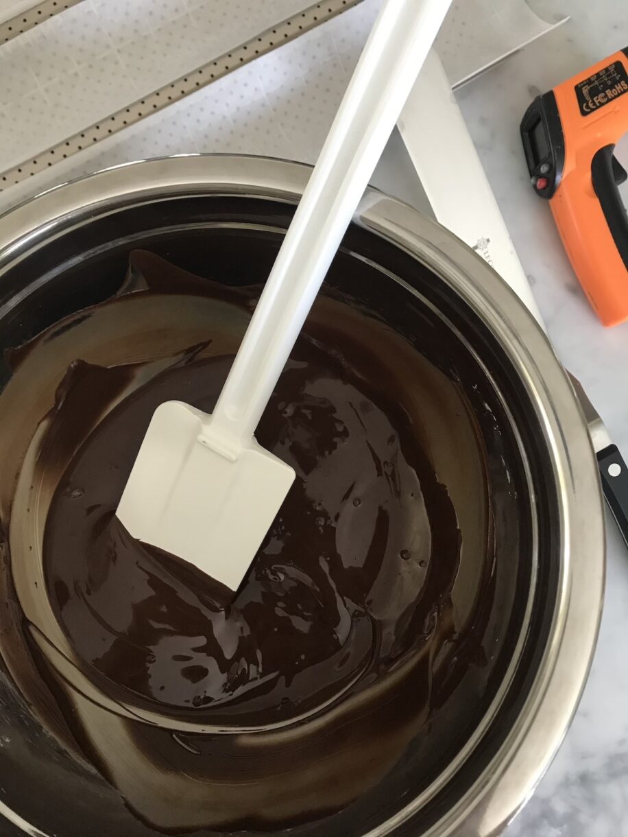Tempering chocolate in a metal bowl, with spatula and thermometer nearby