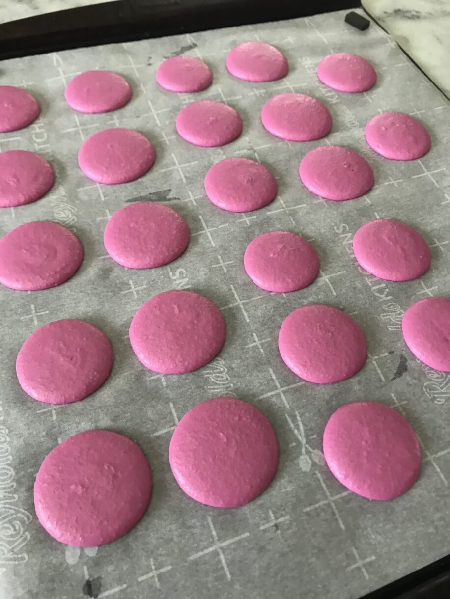 Pink macaron shells piped on a sheet of parchment
