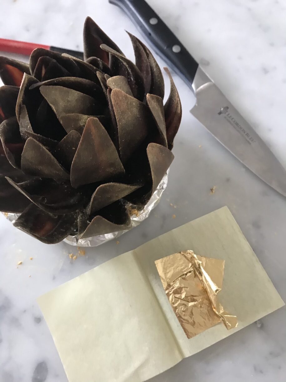 Tempered chocolate rose next to a sheet of gold leaf and a small knife