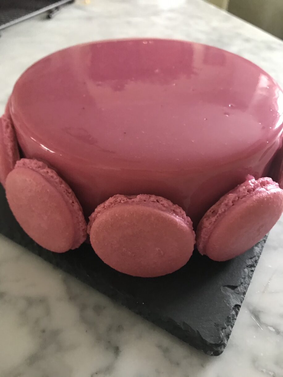 Pink glazed entremet on a marble countertop, with macarons around the edges