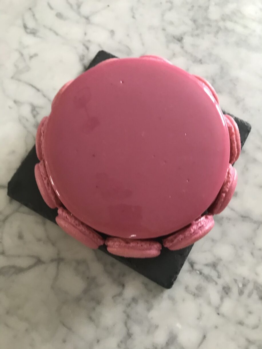 Looking down at a freshly glazed entremet surrounded by macaron shells