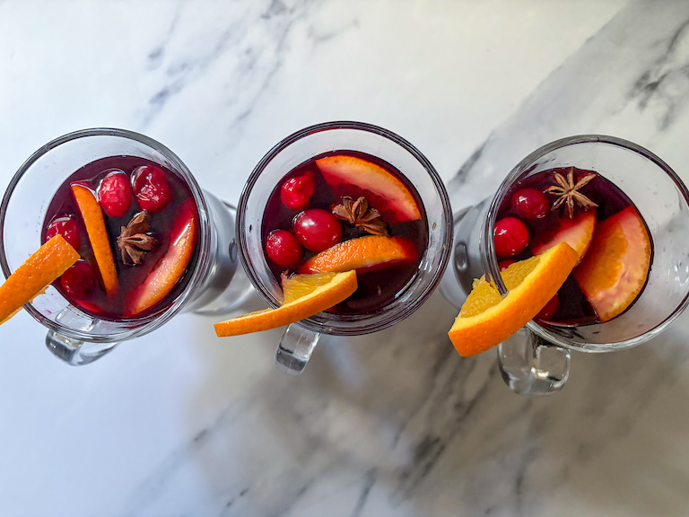 three mugs of mulled wine garnished with cranberries and orange