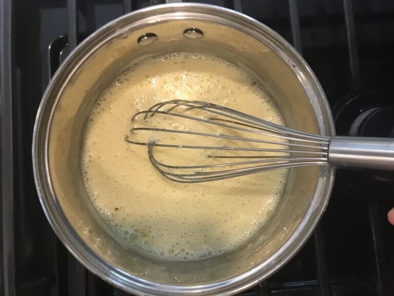 Pastry cream mixture in saucepan on stovetop, with metal whisk