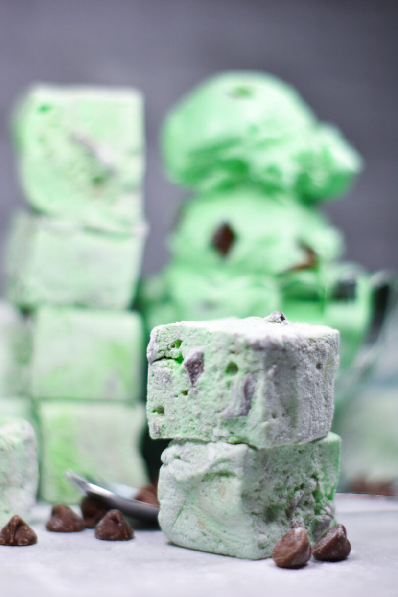 A stack of mint chocolate chip marshmallows in the foreground, with additional marshmallows and scoops of ice cream in the background