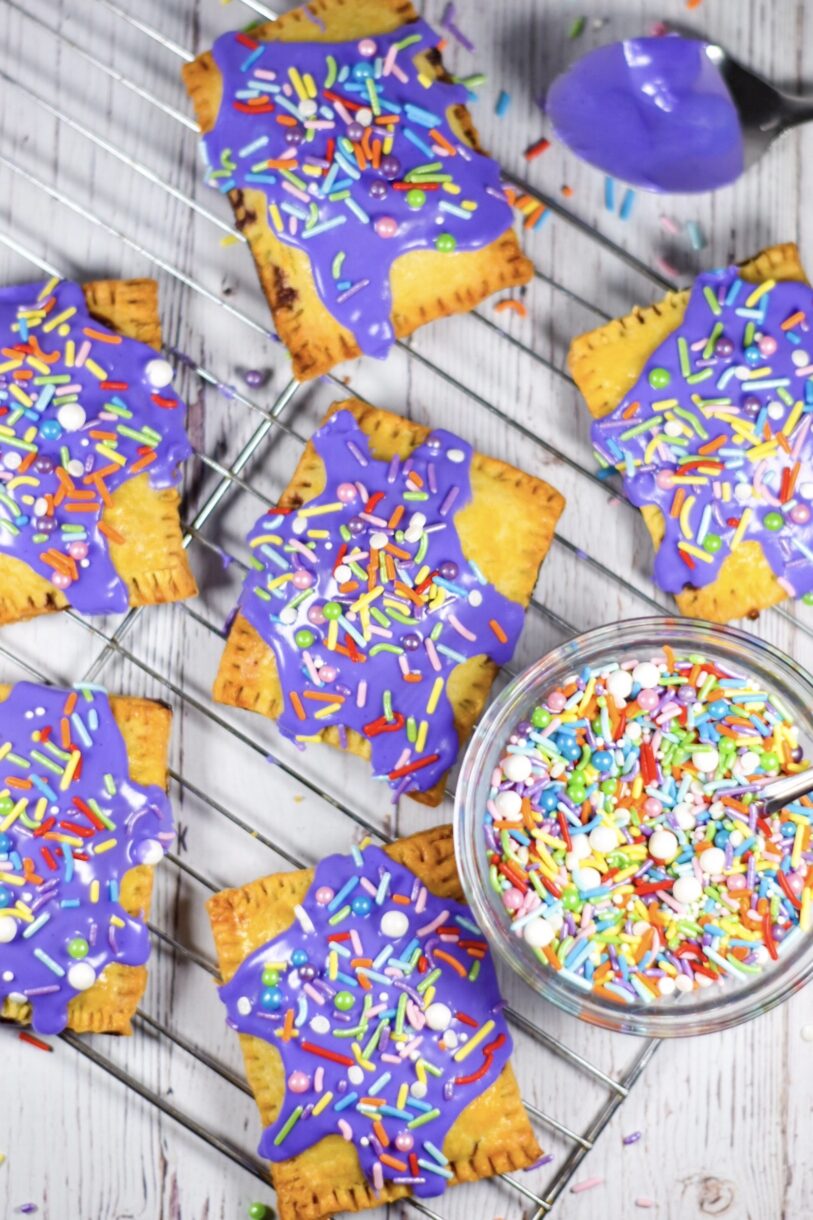 A wire rack with blueberry hand pies and a bowl of rainbow sprinkles