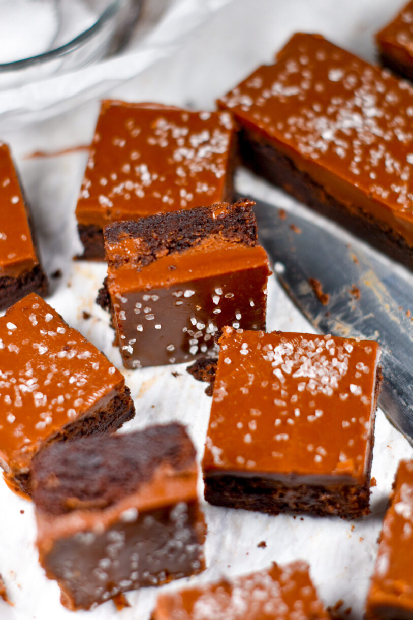 Salted caramel brownies on a white surface, with a knife and bowl of sea salt