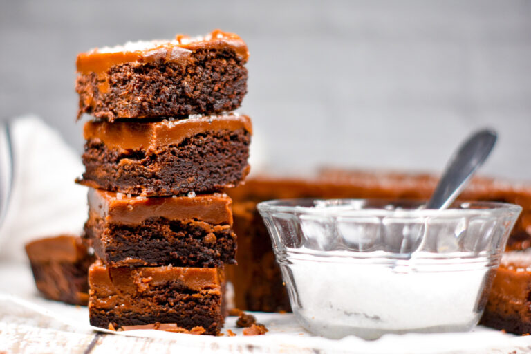 A stack of four brownies and a dish of sea salt with a spoon