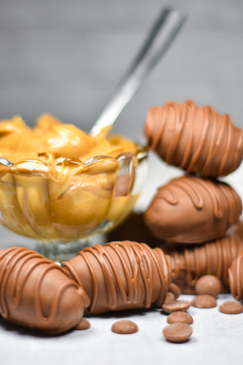 Bowl of creamy peanut butter and a stack of chocolate Easter eggs on a white surface