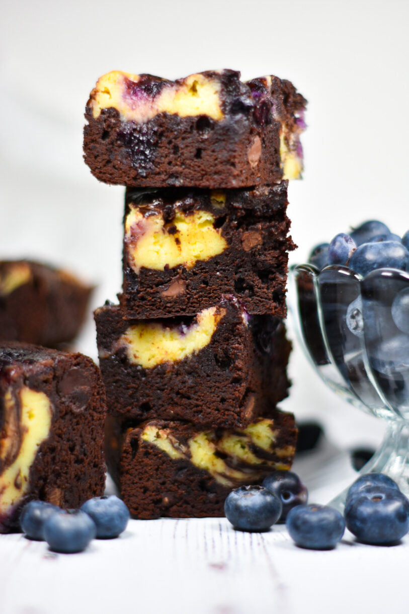 Stack of four blueberry cheesecake brownies next to a bowl of blueberries