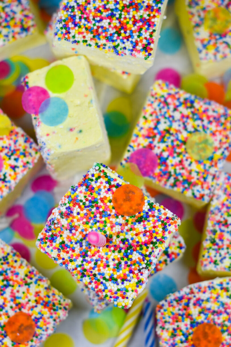 Birthday cake marshmallows with nonpariels, surrounded by candles and colorful confetti, on a white background