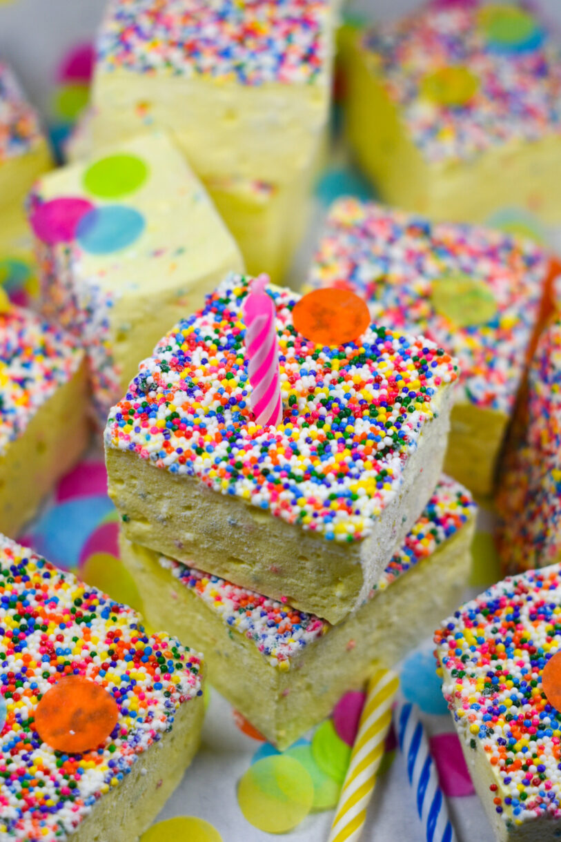 A stack of birthday cake marshmallows, a pink candle, and rainbow confetti
