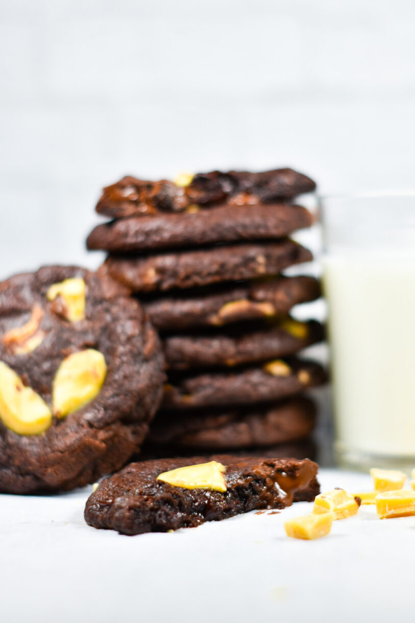 A glass of milk, a stack of passionfruit cookies, and a half cookie with dark chocolate oozing out