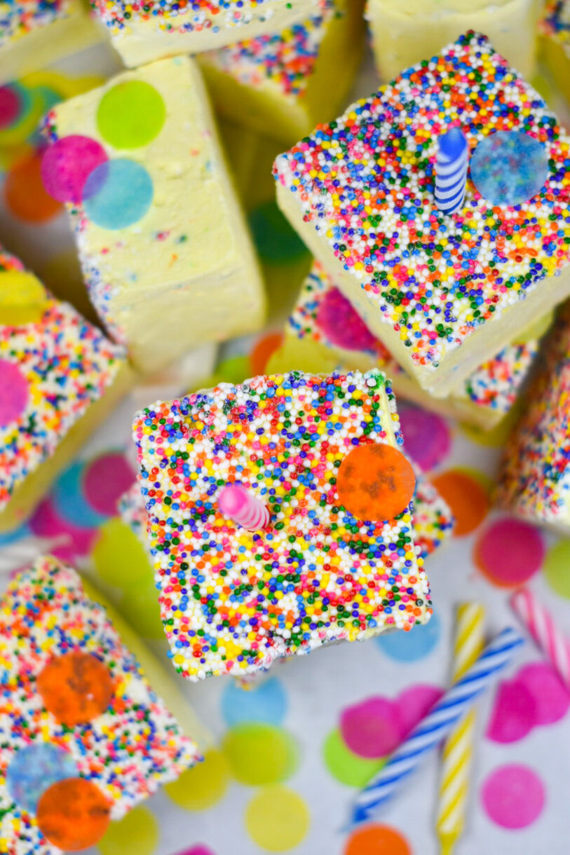 Homemade marshmallows with rainbow nonpariels, surrounded by candles and colorful confetti, on a white background