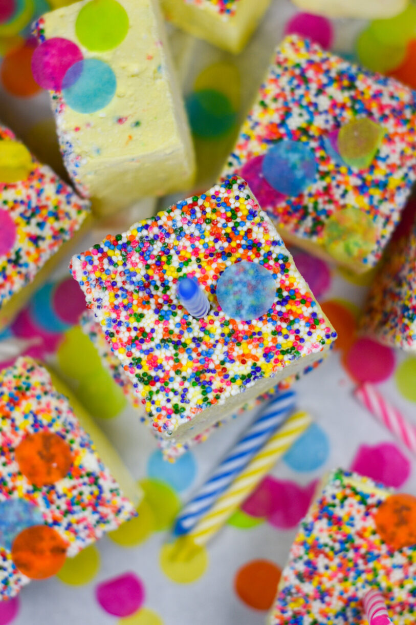 Birthday cake marshmallows with nonpariels, surrounded by candles and colorful confetti, on a white background