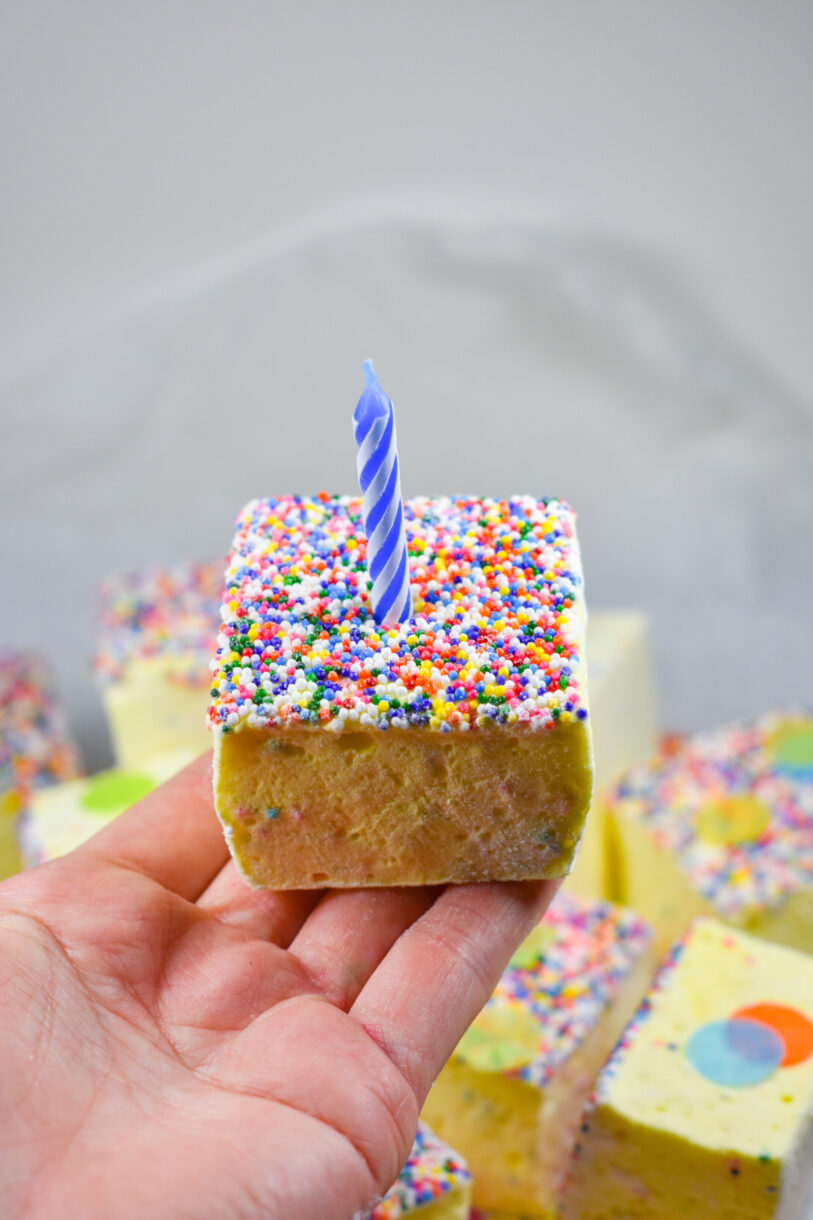 Hand holding a birthday cake marshmallow with a blue candle