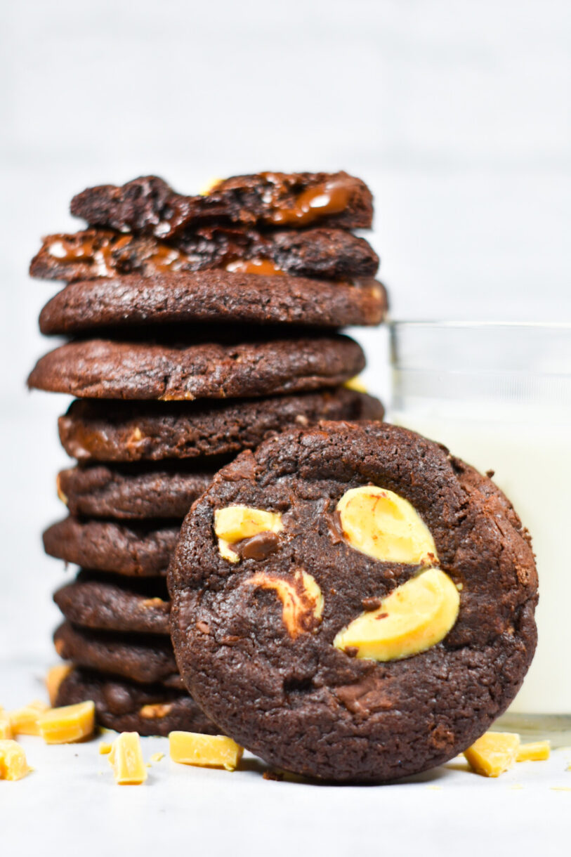 A bakery style chocolate cookie with chunks of passionfruit inspiration, and a glass of milk and cookie stack in the background