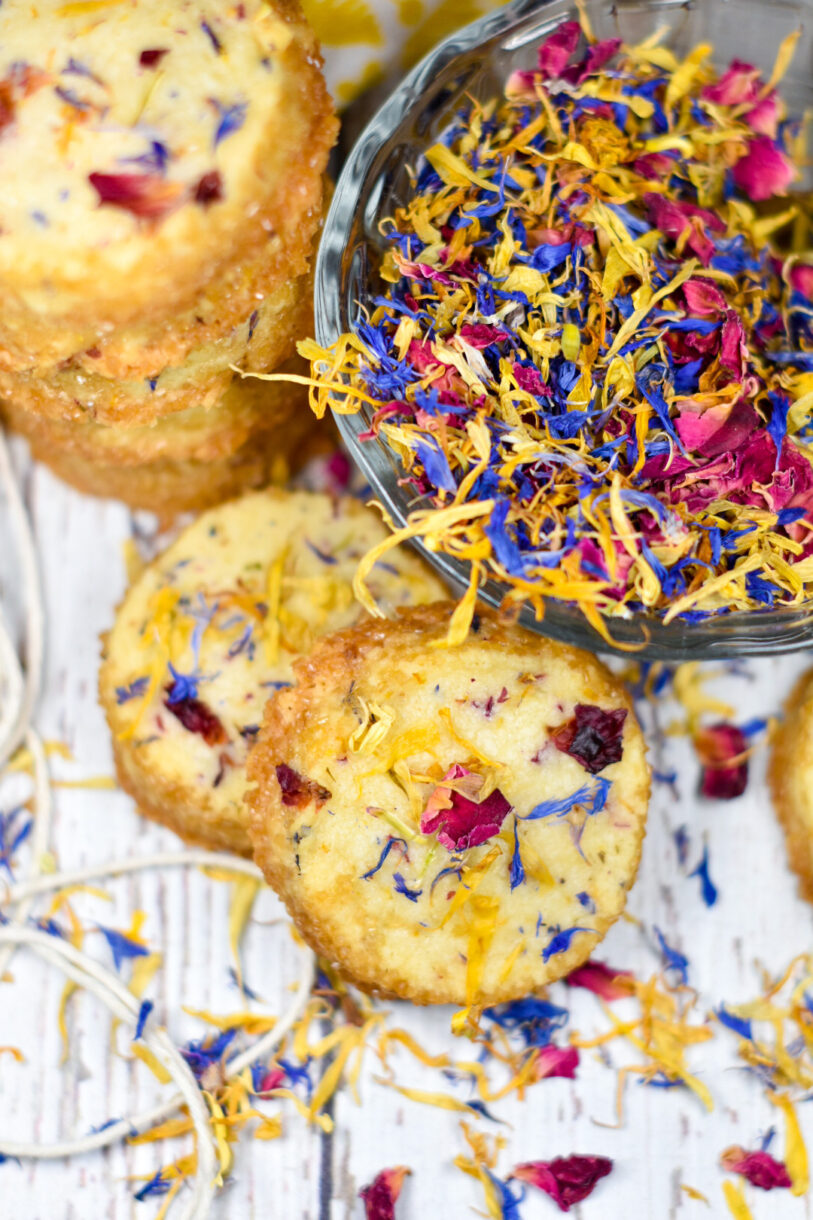 Slice and bake shortbread cookies on a white background, along with a bowl of colorful dried flower petals