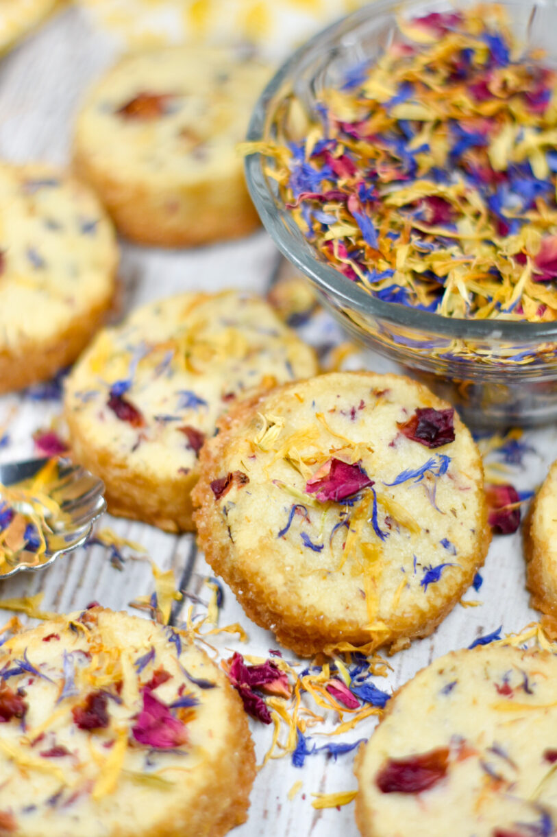 Slice and bake shortbread cookies on a white background, along with a bowl of colorful dried flower petals