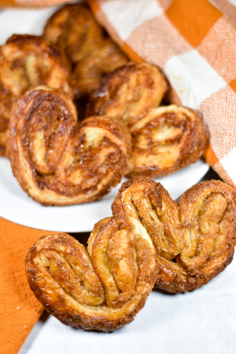 A plate of brown sugar palmiers on a white background, along with orange tea towels