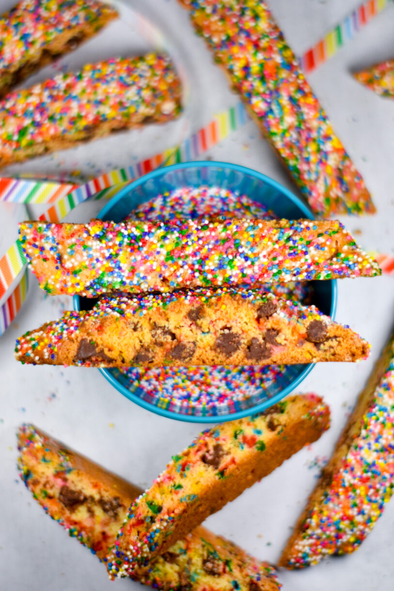Two slices of biscotti balanced on top of a bowl of sprinkles