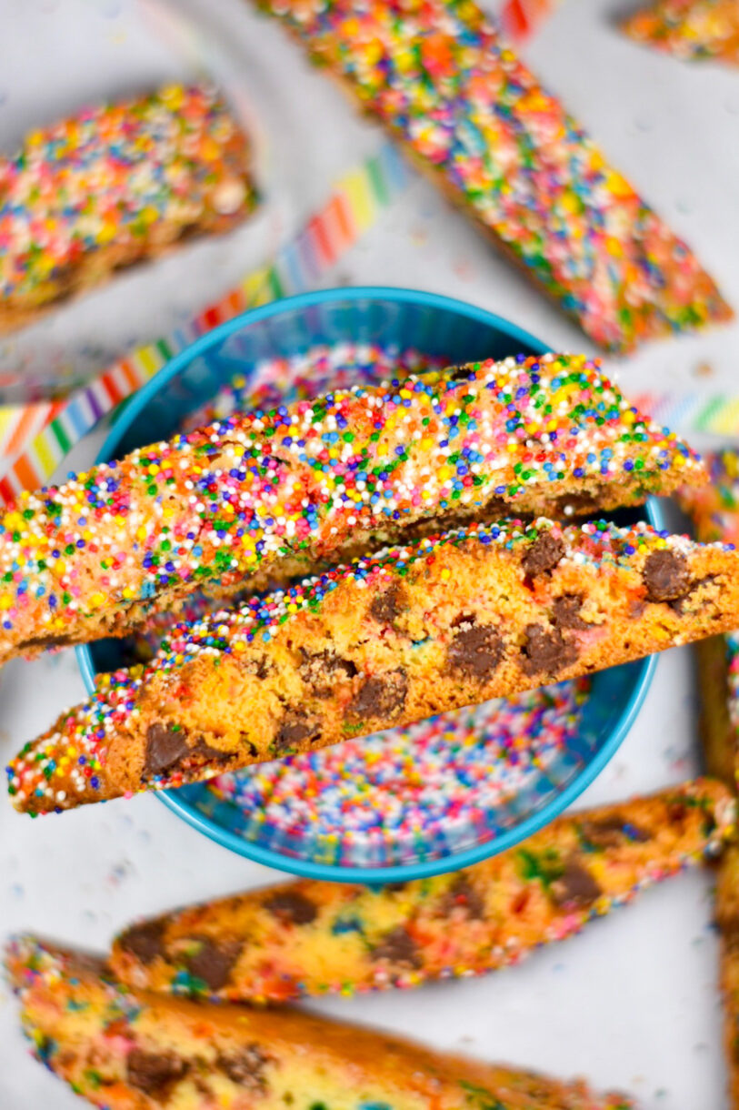 Two chocolate chip cookies sitting on top of a bowl of rainbow sprinkles