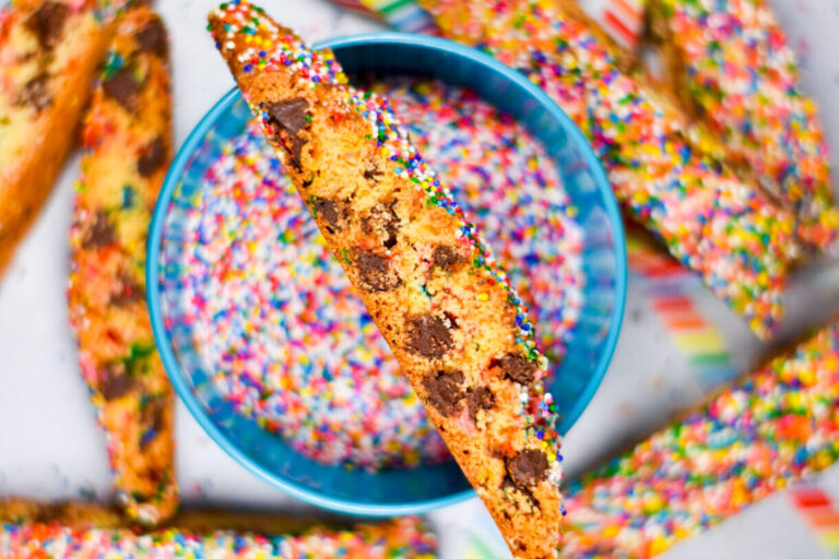 Chocolate Chip Rainbow Biscotti sitting on a bowl of rainbow nonpareil sprinkles