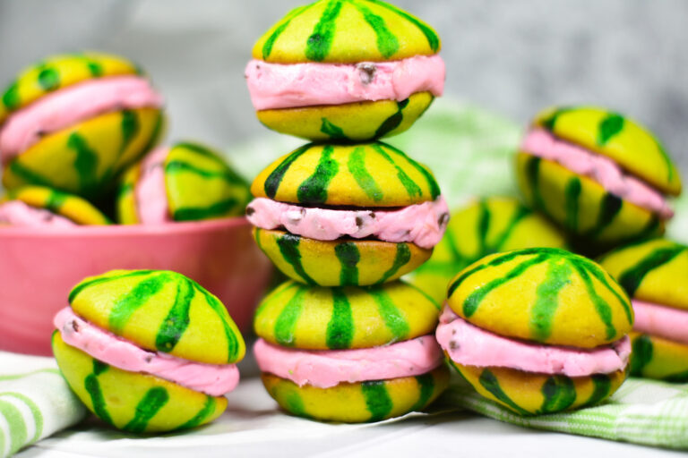 Stack of watermelon whoopie pies with a pink bowl and green towel in the background