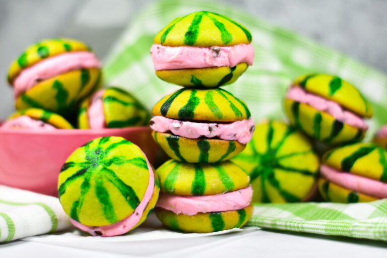 A stack of watermelon whoopie pies, with a pink bowl of whoopie pies and a green plaid towel in the background