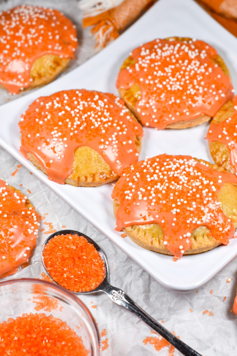 Peach and ginger hand pies on a white plate, with a spoonful of orange sugar nearby
