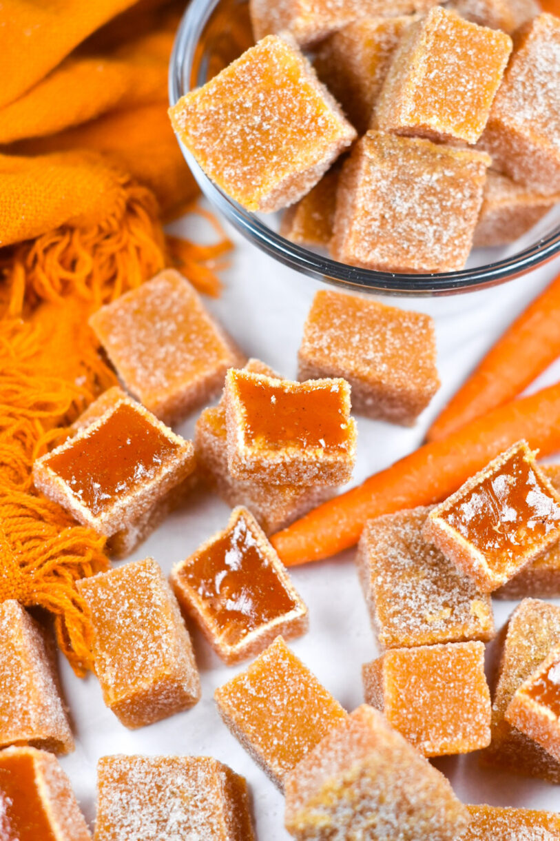 Bowl of carrot candy, carrots, and candy cubes on a white background