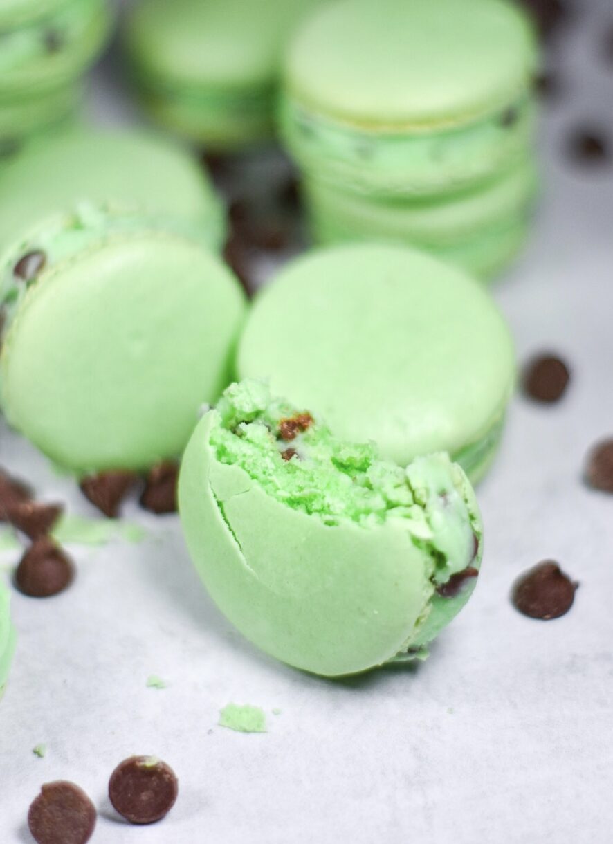 A half eaten mint chocolate chip macaron, with chocolate chips, on a white background