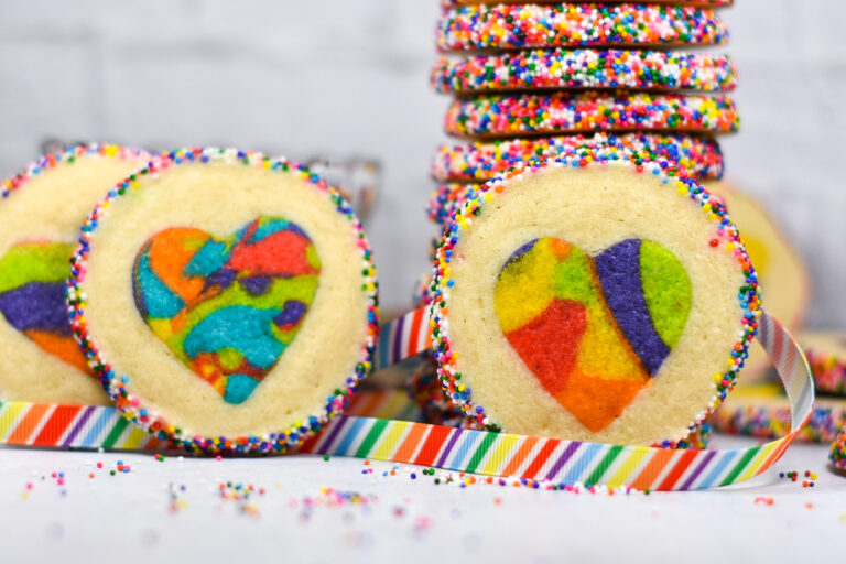 Rainbow Slice and Bake Heart Cookies with striped rainbow ribbon and a cookie stack in the background, surrounded by nonpareil sprinkles