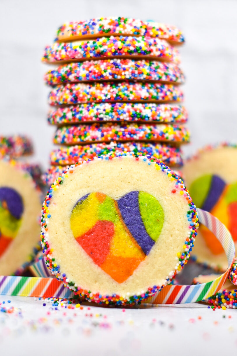 Closeup of a rainbow heart cookie with a stack of cookies in the background