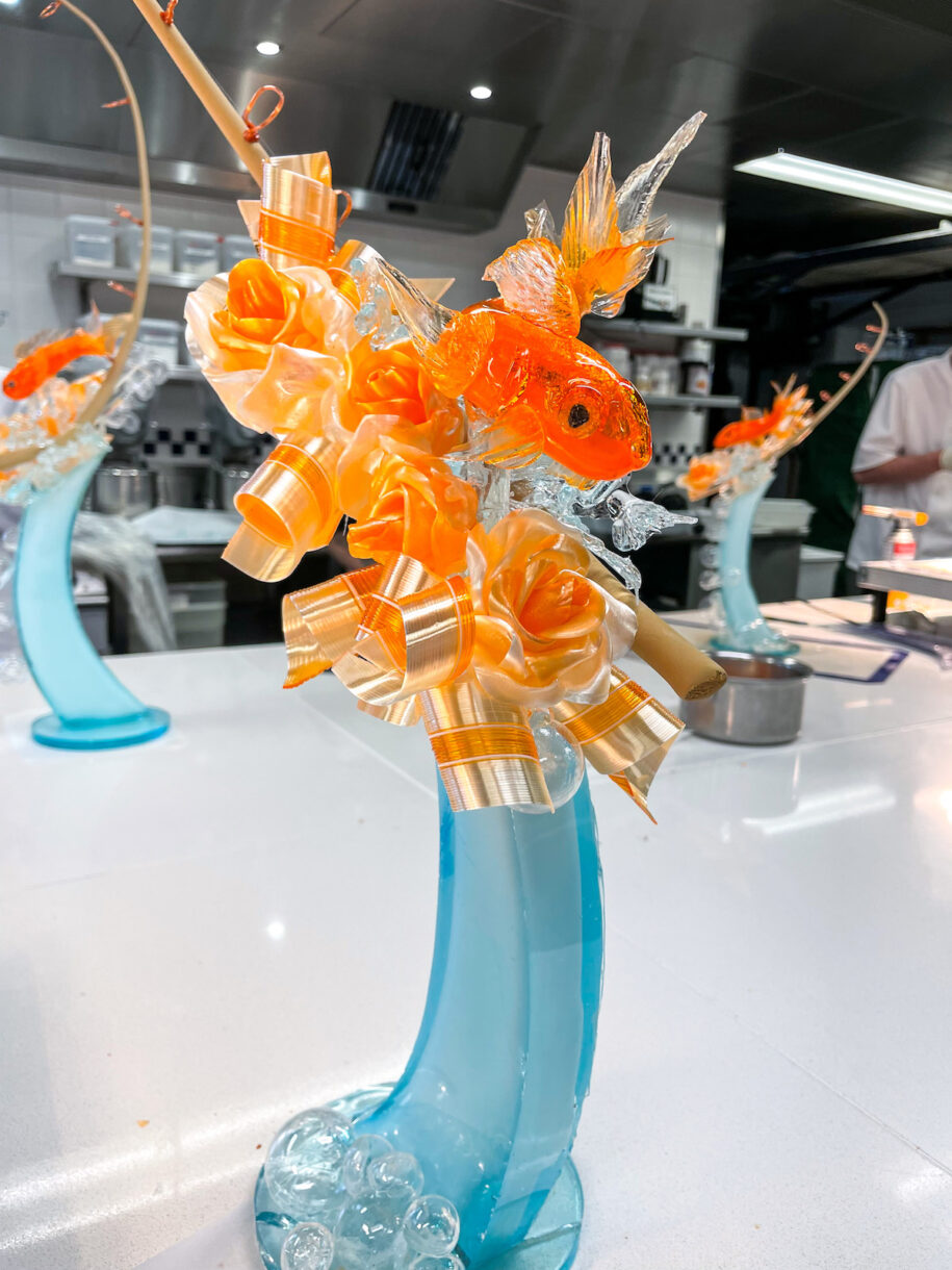A decorative sugarwork sculpture featuring a goldfish, ribbons, roses, and bubbles