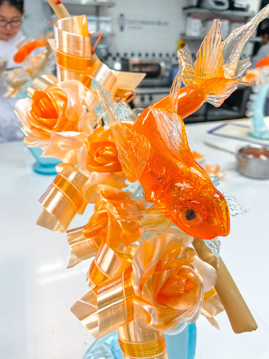 Closeup shot of an orange goldfish, ribbons, and roses made from sugar