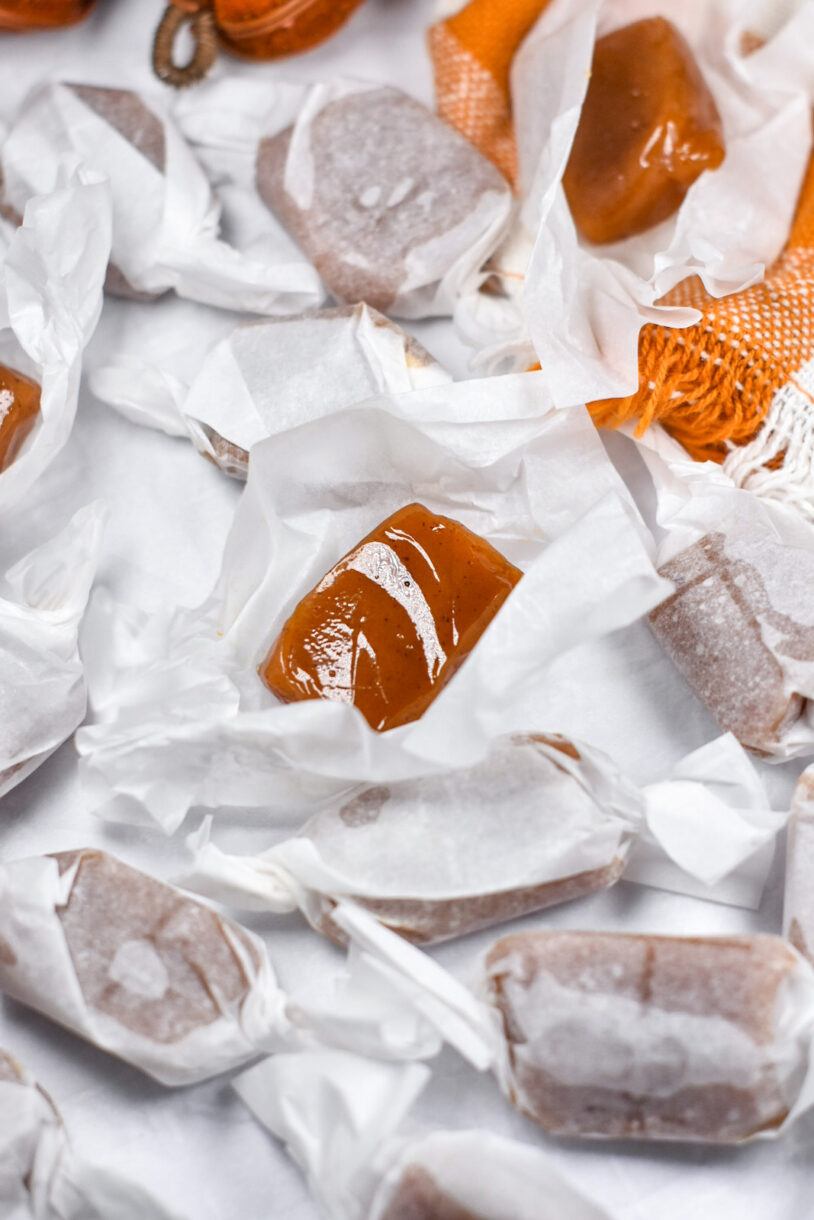 Unwrapped caramel on a square of white parchment, surrounded by wrapped pumpkin caramels