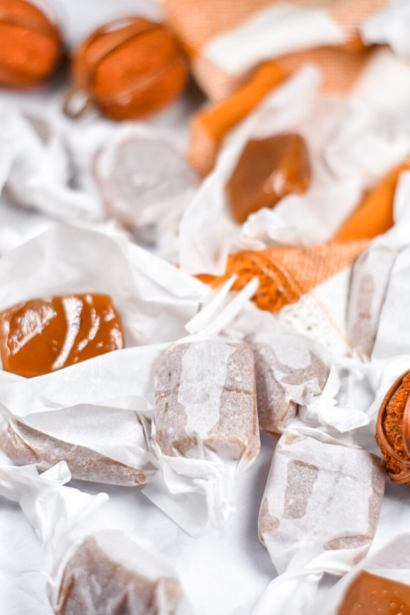 Wrapped and unwrapped caramels surrounded by decorative pumpkins and an orange cloth