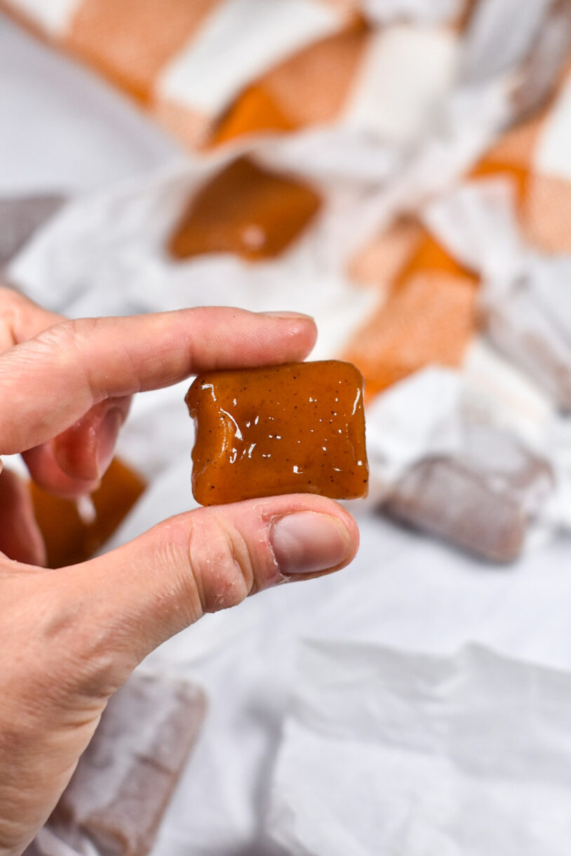 A hand holding an unwrapped caramel candy